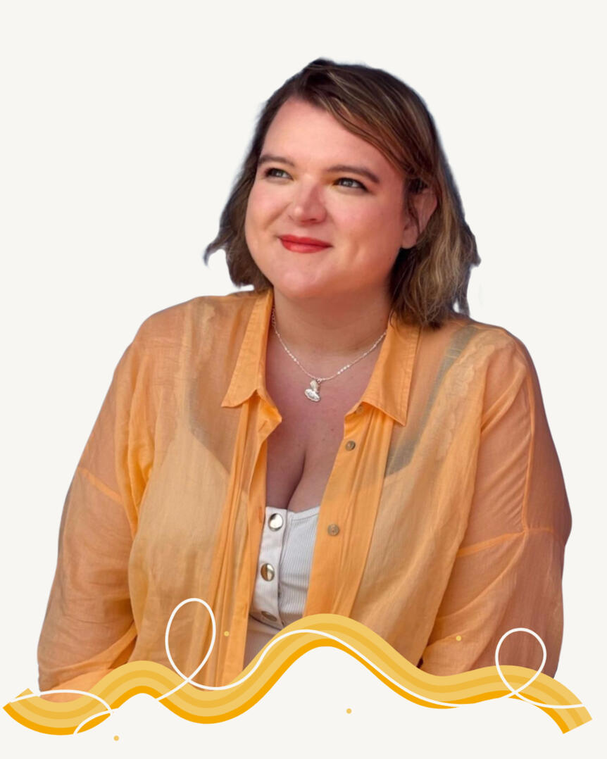 Photo of Becki, owner of Lemon Squeezy Photo of a white woman with shoulder-length dark blonde hair, smiling while looking up and to the right. Wearing a pale orange shirt over a white tank top and a silver necklace with a charm. Image is cut off at the wasit with a wiggly decorative line in sh